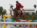 Una jinete montando un caballo en una competencia de salto, saltando sobre un obstáculo colorido.