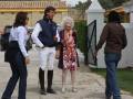 Una anciana con un vestido floral y sandalias se dirige a una joven pareja en ropa deportiva, mientras otra persona observa desde atrás.