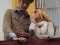 Un hombre y una mujer en un balcón, ella cubriendo su boca con la mano, ambos vestidos con ropa casual.