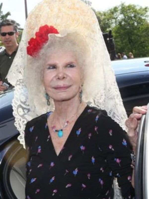 Elegant woman in traditional Spanish mantilla and floral dress, arriving at an event.
