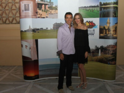 Un hombre y una mujer posan frente a un mural de imágenes turísticas, incluyendo edificios históricos y paisajes naturales.