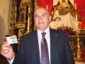 Un hombre en traje sostiene una tarjeta con el logo de Microsoft, frente a un altar con una imagen religiosa en el fondo.