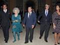Una familia elegante camina juntos en un ambiente formal. El padre, con corbata azul, lleva una chaqueta y pantalones oscuros. La madre, con vestido verde y zapatos azules, sostiene un bolso. Los otros dos adultos también llevan trajes y chaquetas. La escena transmite una sensación de respeto y solemnidad.