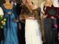 Una mujer en un vestido azul sostiene una placa mientras otras personas la observan.