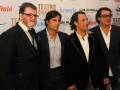 Cuatro hombres en trajes posando juntos en un evento de teatro.