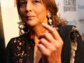 A una mujer con cabello largo y ondulado, llevando un vestido negro con detalles en crochet. El fondo contiene varios logotipos y textos, incluyendo "Teatro Donizetti".
