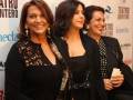 Tres mujeres sonríen en un evento de teatro, vestidas con elegancia y sonriendo hacia la cámara.