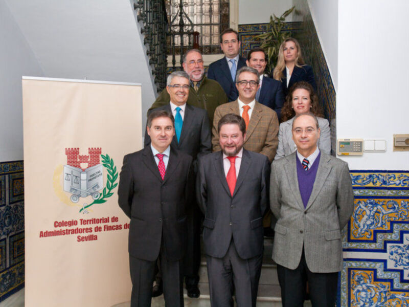 Grupo de personas en trajes posando frente a un cartel con el logo del Colegio Territorial de Administradores de Fincas de Sevilla.