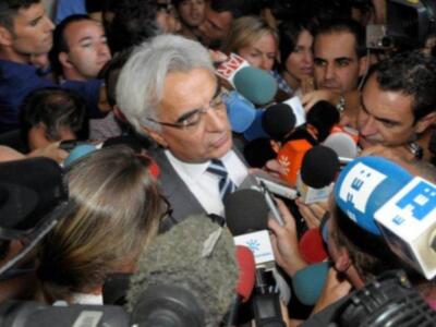 El fotógrafo captura a un político en medio de una conferencia de prensa, rodeado por micrófonos de diferentes medios. La escena está llena de actividad y concentración, reflejando la importancia del evento.