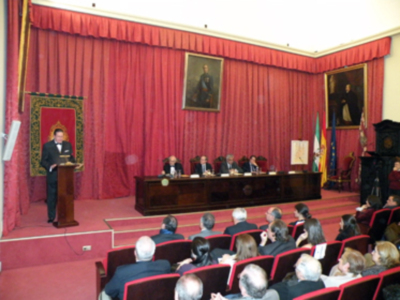 Sala de audiencias con cortinas rojas, sillas para los asistentes y una persona en el escenario.