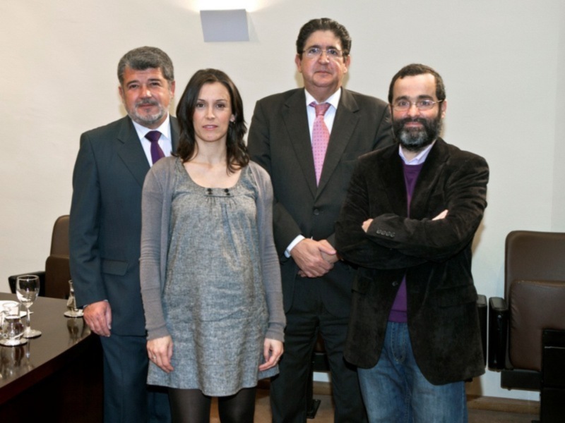 Reunión de negocios en un entorno formal con dos hombres y una mujer en trajes y una mujer en vestido casual.