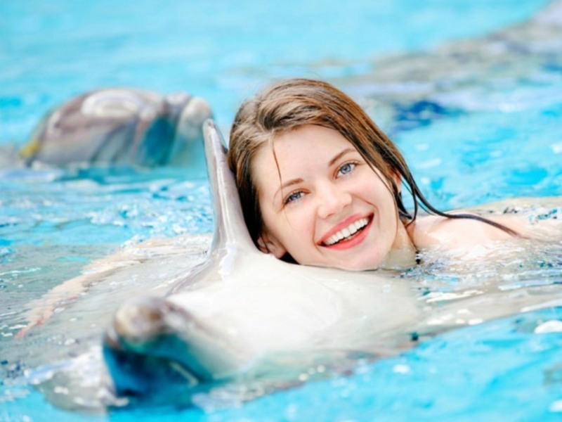 Mujer sonriendo mientras nada con un delfín en una piscina.