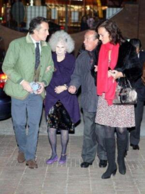 Una imagen de una persona vestida con un abrigo verde y pantalones azules, otra con un vestido largo y tacones altos, una tercera con una chaqueta estampada y botas de cuero, y la última con un vestido largo y tacones altos. Todos están caminando por una calle iluminada con luces de fondo y un edificio en el fondo.