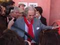 Una persona en un traje azul y una bufanda roja, rodeada de personas con cámaras y otros fotógrafos.