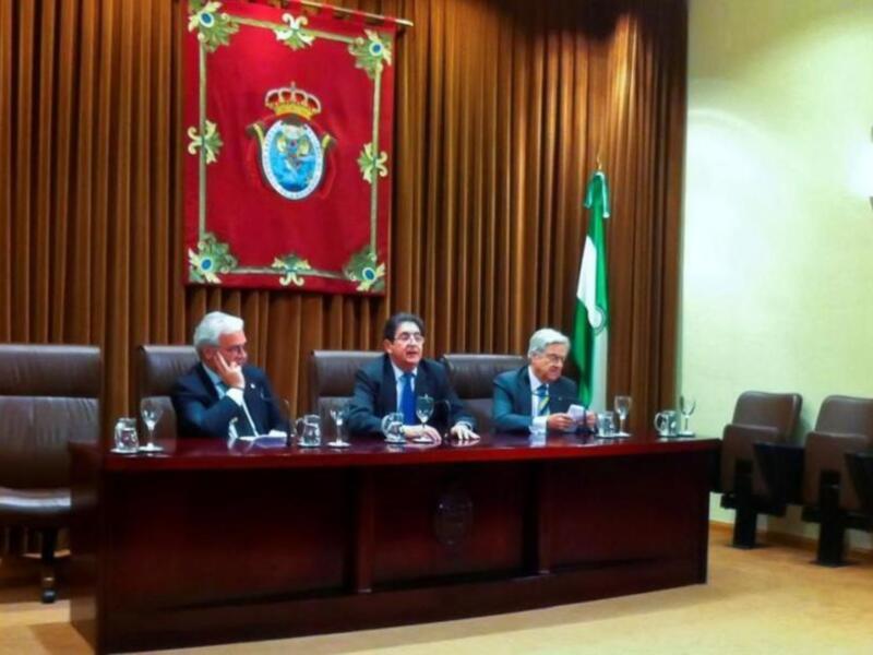 Reunión oficial en un salón con bandera y escudo en el fondo.