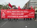 Mujeres y hombres sostienen una pancarta roja con el lema "Por el Frente Único del Pueblo, por el Socialismo. Proletarios del Mundo, Uníos!". La pancarta incluye logos de organizaciones políticas como PCOE y FICE.