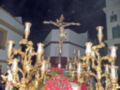 Un crucificado dorado en el centro, rodeado por candelabros y flores rojas. Fondo blanco con detalles dorados, iluminación nocturna.