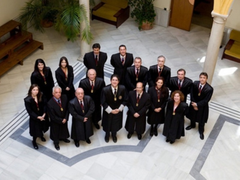 Equipo de profesionales en un entorno formal, posando para una foto en una sala con suelo de mármol y plantas en el fondo.