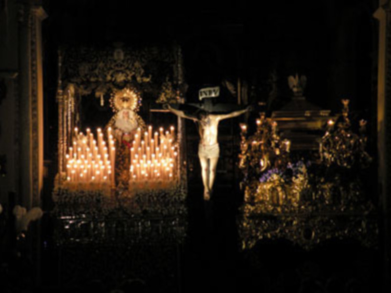 Procesión religiosa con la imagen del Cristo de la Buena Muerte en el centro, rodeado de velas y ornamentos dorados.