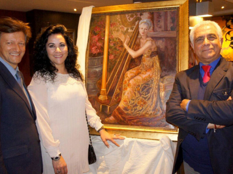 Tres personas posan junto a un retrato de una mujer tocando la arpa, en un ambiente formal y artístico.