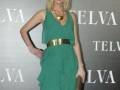 Una mujer con cabello largo y rubio, vestida de verde con un cinturón dorado. Posa en una alfombra roja frente a un fondo con el logo de Telva y Selva.