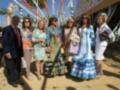 Una familia en trajes tradicionales de la Feria de Abril, posando frente a un escenario festivo con banderas y decoraciones.