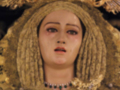 Imagen de una figura religiosa vestida con un manto dorado y joyas, posiblemente representando a una santa o virgen. La figura lleva un tocado ricamente adornado con piedras preciosas y una corona. La imagen parece estar en un entorno de iglesia o templo, con detalles arquitectónicos que sugieren una atmósfera de reverencia y veneración.