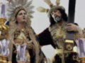 Imagen de una procesión religiosa con dos personajes vestidos en trajes tradicionales, uno lleva una cruz y el otro sostiene un candil.