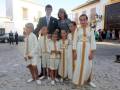 Una familia posa para una foto en una calle adoquinada, con niños vestidos con trajes blancos y dorados, posiblemente durante una celebración religiosa o tradicional.