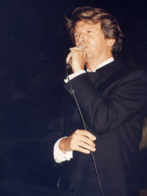 Persona en traje negro cantando en un escenario.