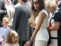 Una mujer con vestido blanco y gafas de sol, caminando entre una niña pequeña y un niño pequeño. Algunos adultos están detrás de ellos, algunos con cámaras.