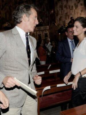 Un hombre en traje beige hablando con una mujer sonriente, ambos están frente a un piano.