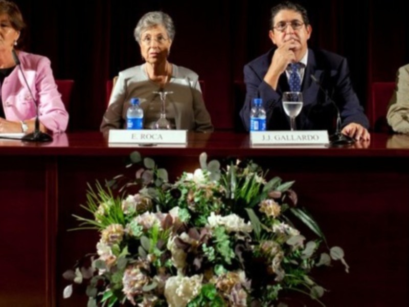 Panel de expertos en una conferencia, sentados detrás de un escritorio con nombres de participantes.