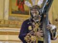 Un Cristo crucificado en una iglesia, vestido con un manto negro y una corona de espinas. En el fondo, se puede ver una pintura religiosa que representa a un santo. La escena transmite la espiritualidad y el dolor de Cristo durante su crucifixión.