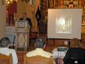 Una sala de conferencias con un hombre hablando frente a una pantalla proyectando una imagen de una iglesia.