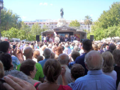 Una multitud en un evento al aire libre, con una escultura en el centro y palmeras alrededor.