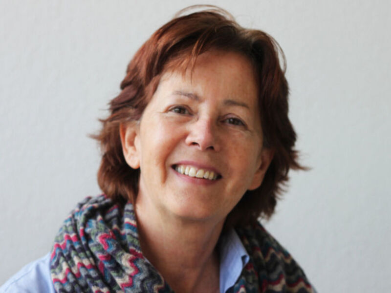 Retrato de una mujer sonriente con cabello castaño y bufanda multicolor, fondo blanco.