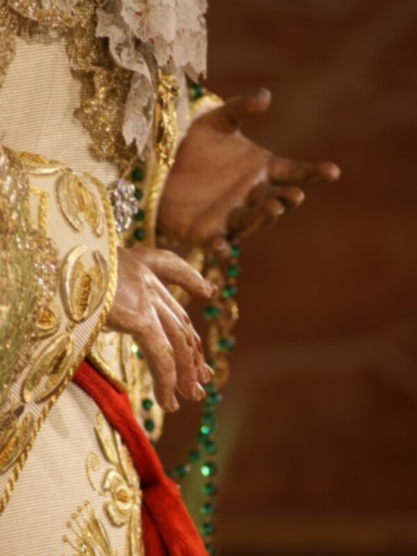 Manos con joyas y vestimenta dorada, probablemente en una celebración religiosa o tradicional.