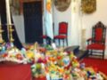 Una mesa cubierta con una manta roja llena de bolsas de comida y productos diversos, en un ambiente decorado con cortinas azules y sillas rojas.