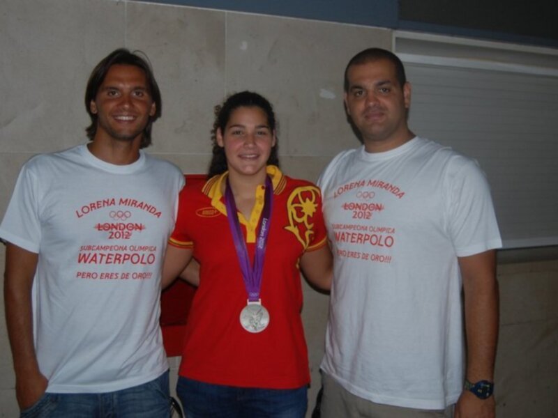 Tres personas sonrientes posan con camisetas de waterpolo, uno con una medalla.