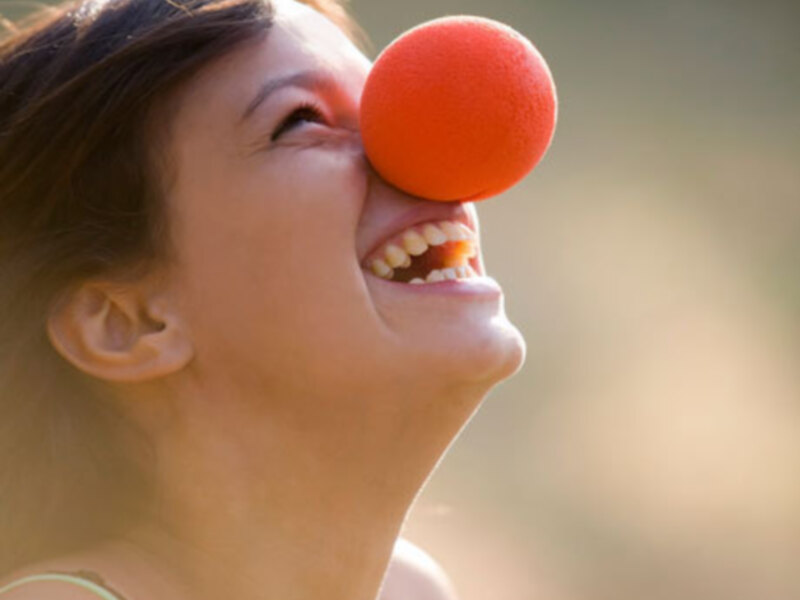 Una mujer con una pelota de espuma roja en la nariz, riendo y disfrutando del momento.