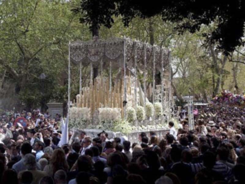 Una procesión religiosa con una carroza decorada con flores y adornos, rodeada de una multitud en un ambiente festivo.