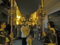 Procesión nocturna con velas y vestimentas tradicionales en una calle iluminada.