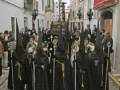 Desfile religioso en una calle de la ciudad, con personas vestidas con trajes tradicionales negros y sombreros.