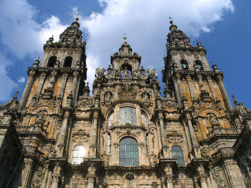 La Catedral de Santiago de Compostela, una de las catedrales más famosas y majestuosas del mundo. Su arquitectura gótica es impresionante, con dos torres altas y ornamentadas. El cielo azul con algunas nubes lo complementa perfectamente, destacando la belleza de esta icónica estructura.