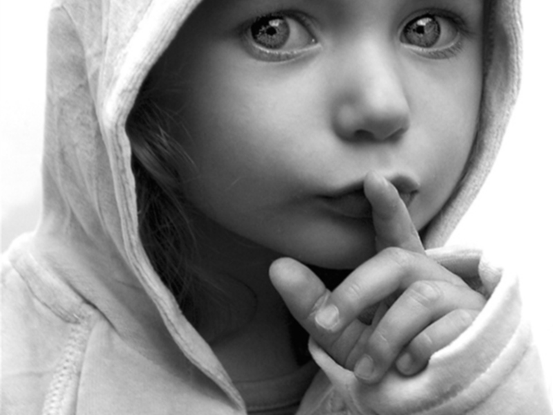 Una niña con una capucha blanca, mirando directamente a la cámara. Su expresión es seria y pensativa.