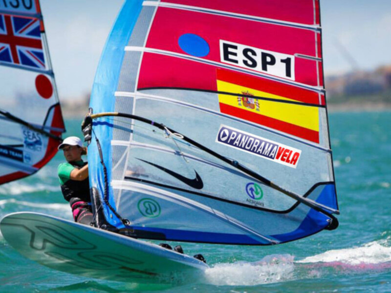 Sailboarder en acción con bandera española y logotipo de Panorama Vela.