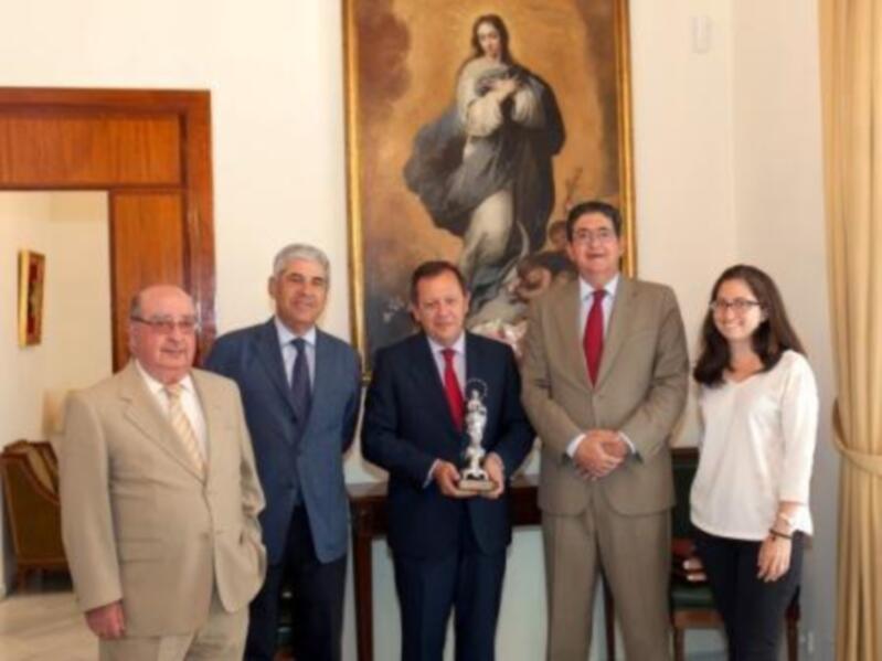 Celebración de un evento con un grupo de personas en trajes formales, uno de ellos sostiene un trofeo, en un entorno formal con un retrato de Jesús en el fondo.