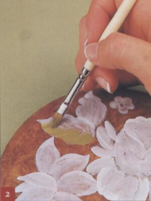Una mano sosteniendo un pincel de acuarela, aplicando pintura sobre una superficie con dibujos de flores en un estilo delicado y detallado.