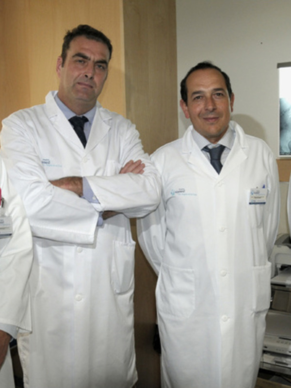 Cuatro médicos en trajes blancos sonrientes y confiados en un entorno clínico.